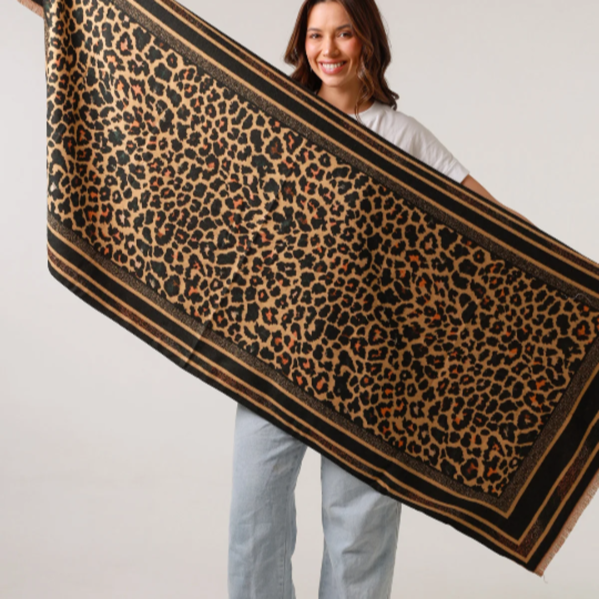 Woman holding a large leopard print scarf against a plain background