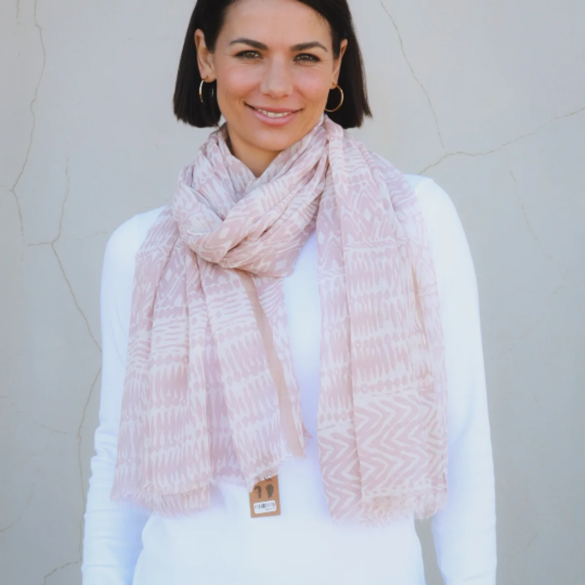 Woman wearing a light taupe brown scarf and white sweater against a plain background