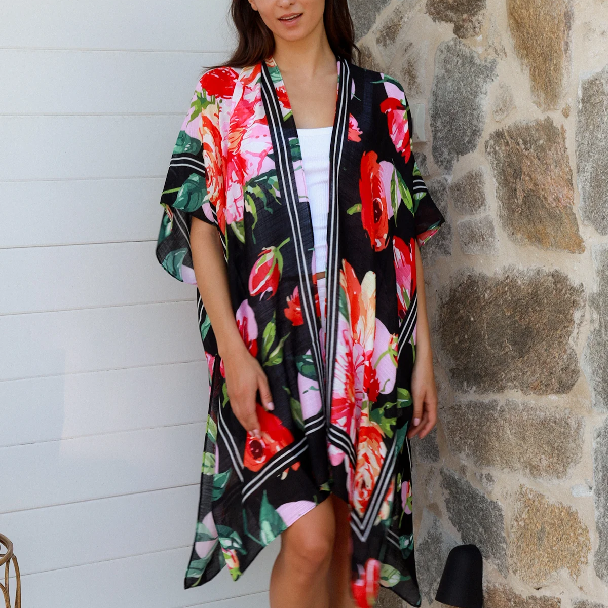 Woman wearing a colorful floral kimono standing against a stone wall.