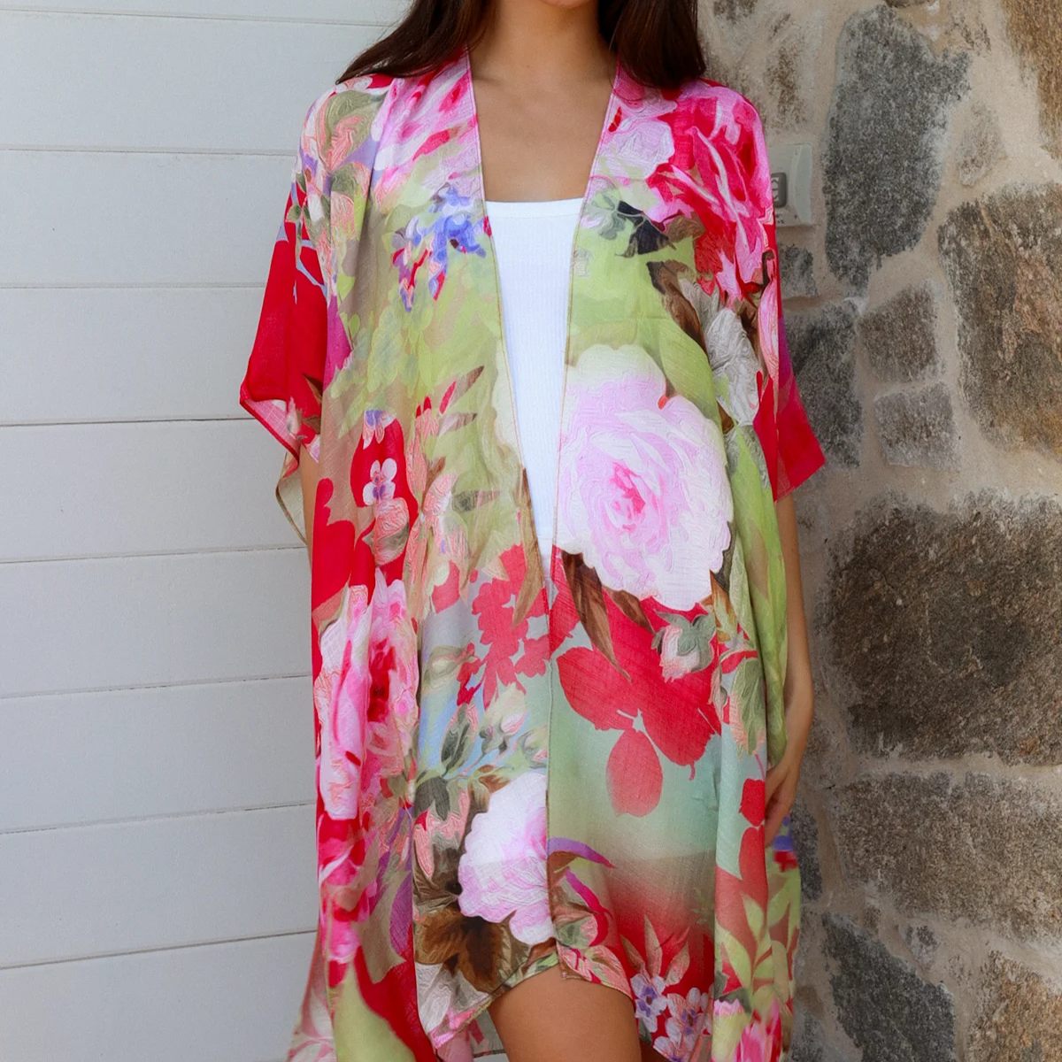 Woman wearing a colorful floral kimono standing against a stone wall.
