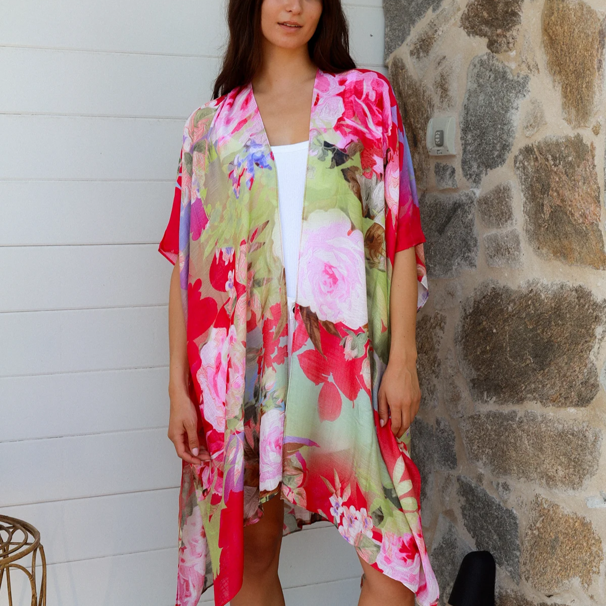 Woman wearing a colorful floral kimono standing against a stone wall.