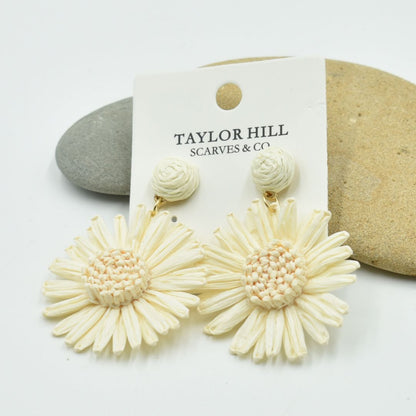 Cream-colored floral earrings on a Taylor Hill branded card with stones in the background