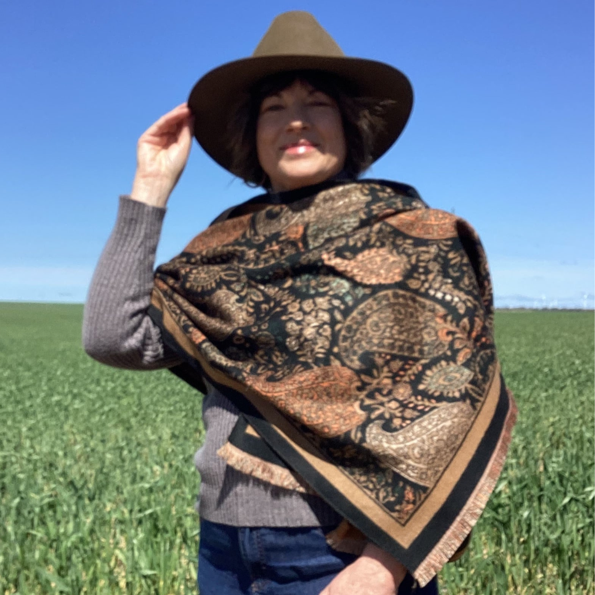 A lady wearing a patterned scarf and hat in a field
