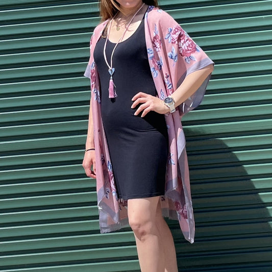 Woman wearing a black dress and pink floral kimono against a green corrugated metal background