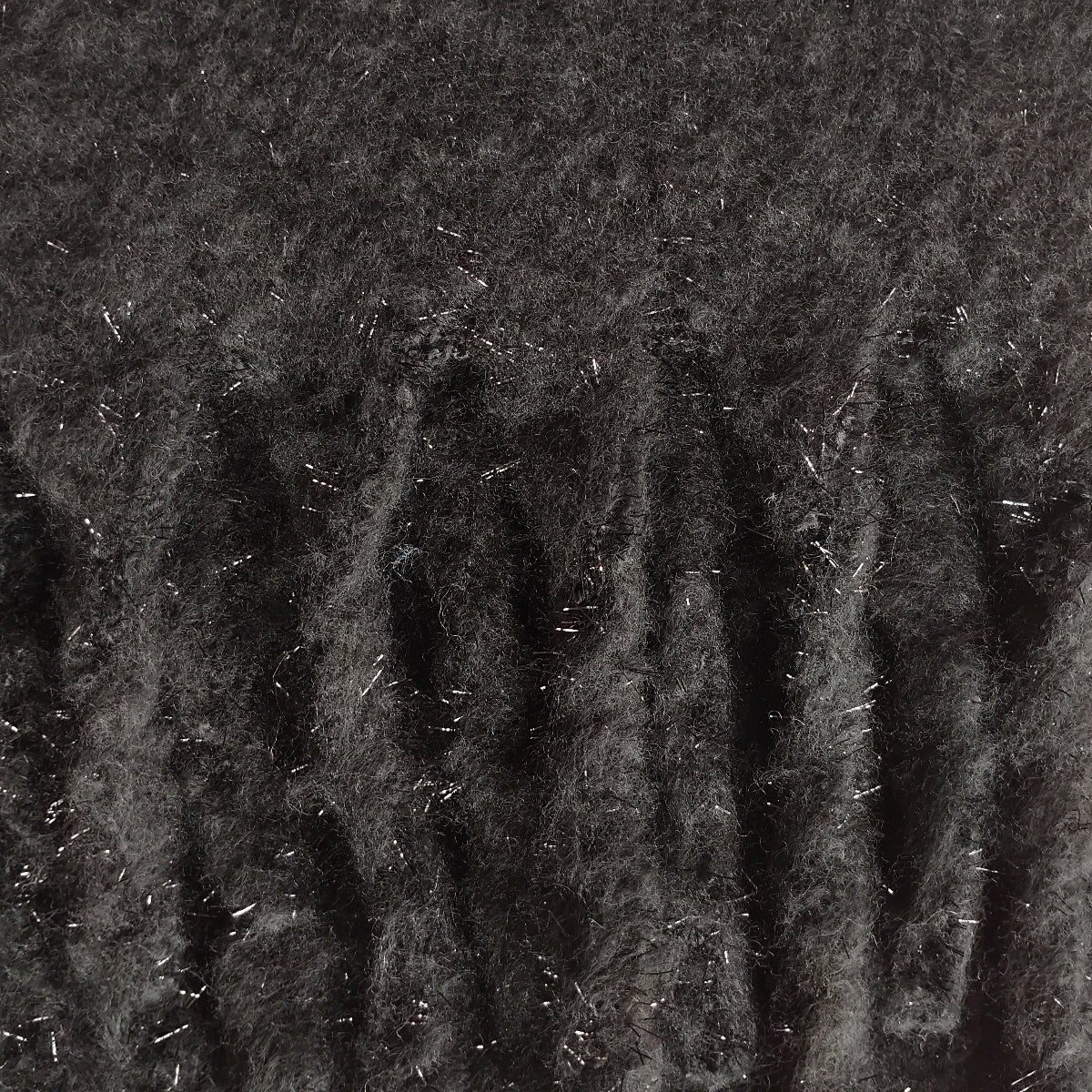 Close-up of soft and warm black knit scaf with a silver metallic thread and chunky tassels