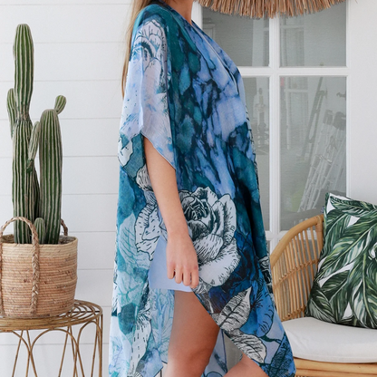Woman wearing a blue floral kimono standing in a tropical setting with a cactus and outdoor furniture.