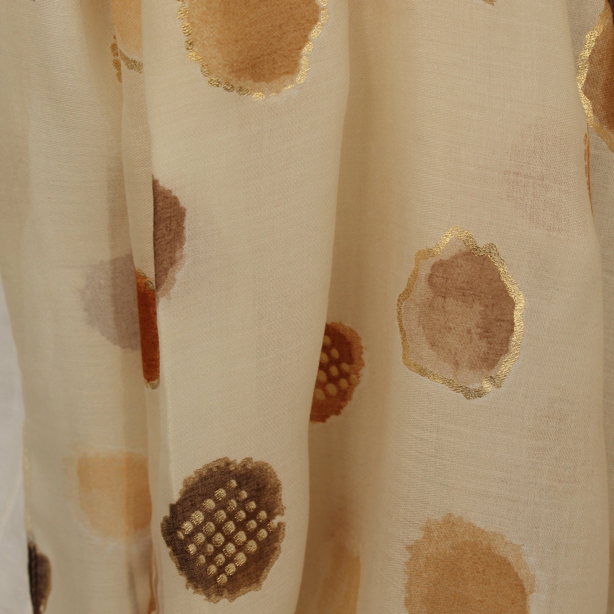 A close-up of a cream-colored sheer scarf with metallic gold and brown watercolor-style circular patterns.