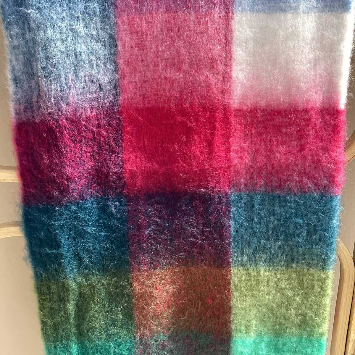 A close-up of a plaid scarf or wrap with vertical and horizontal stripes in blue, pink, green, brown, and white.