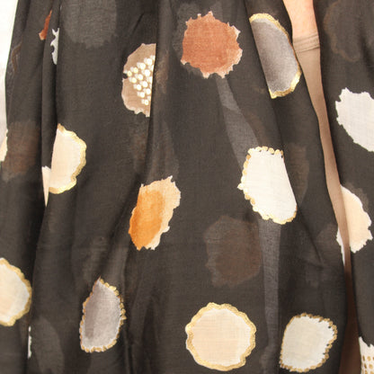 A close-up of a black scarf featuring a pattern of irregular watercolor-style polka dots in beige, white, brown, and gray.