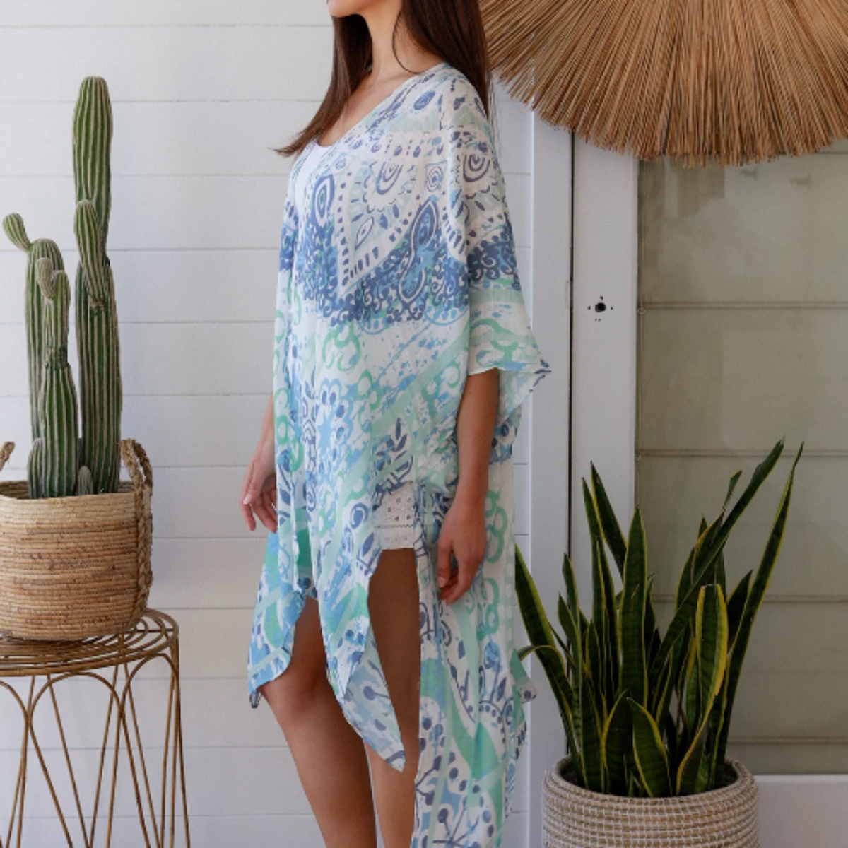 Woman wearing a blue kimono standing in a room with plants and a woven basket.