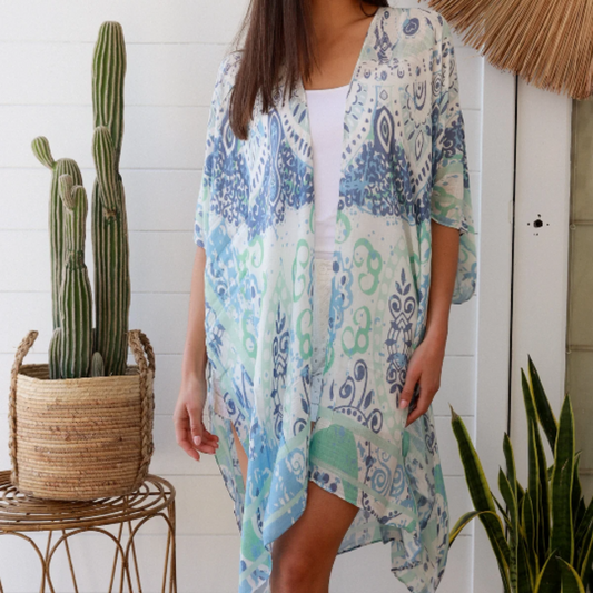 Woman wearing a patterned kimono standing in front of a white wall with plants.