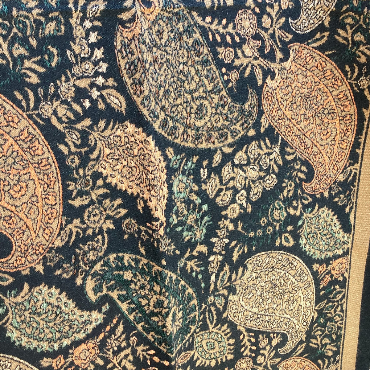 Close-up of a patterned ladies scarf that has a paisley designs in caramel brown and green on a dark background.