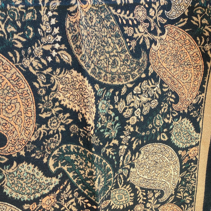 Close-up of a patterned ladies scarf that has a paisley designs in caramel brown and green on a dark background.