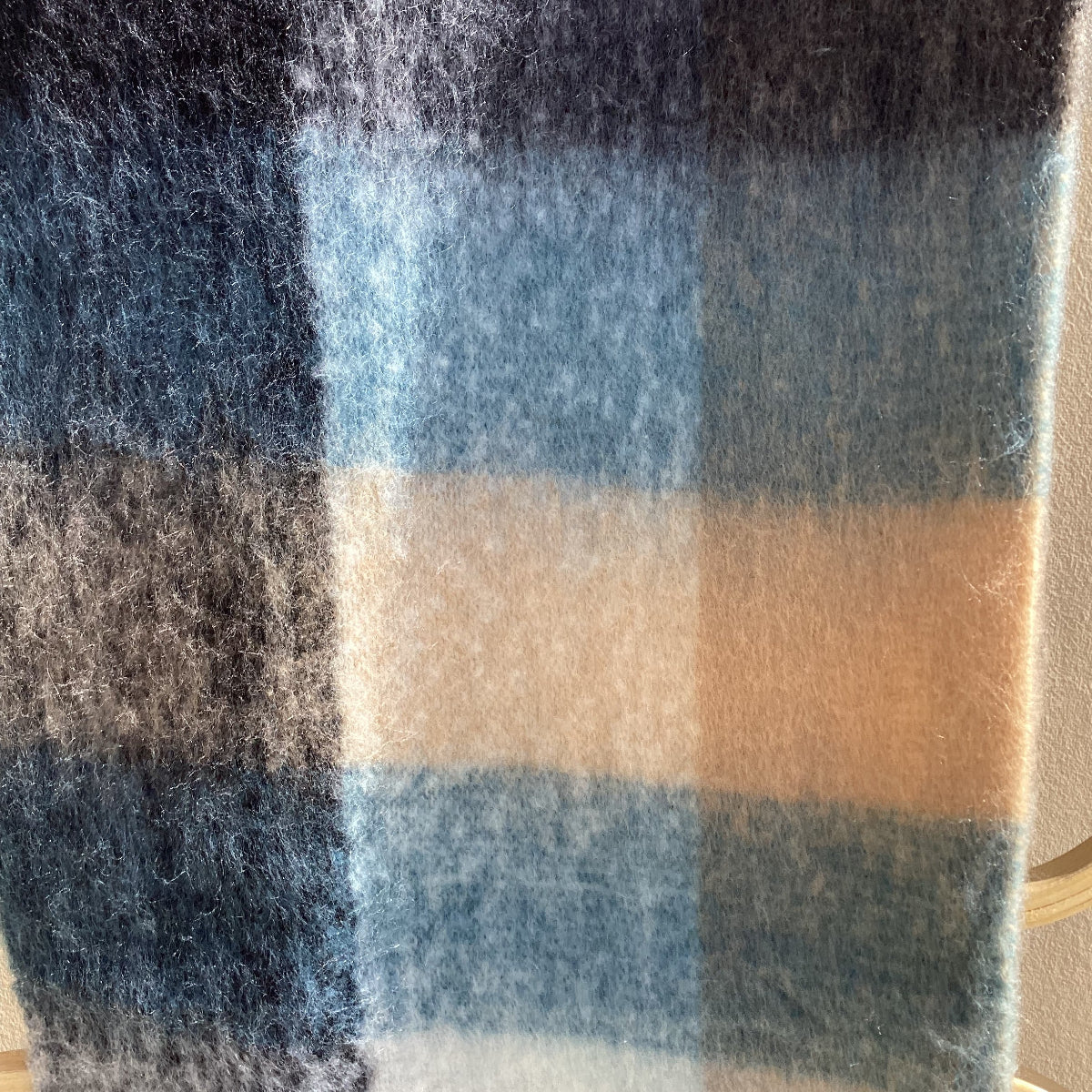 A close-up of a soft, fuzzy plaid fabric or scarf in muted blue, beige, white, and dark charcoal tones.
