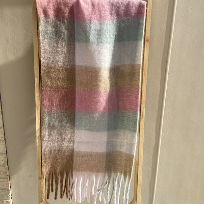 A soft woven scarf with a plaid pattern in dusty pink, sage green, beige, and white, draped over a minimalist gold metal frame against a neutral beige wall.