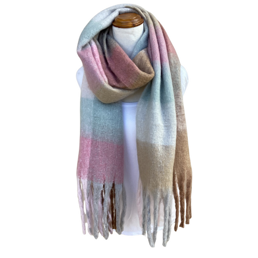 A soft, oversized striped scarf with fringe ends, draped on a white mannequin torso. The scarf features horizontal stripes in dusty pink, light blue, beige, and light brown, with a gradient fade toward the bottom.