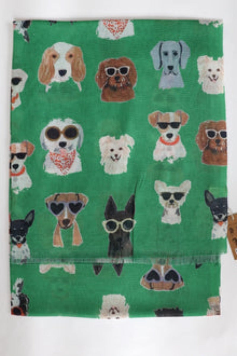 a ladies scarf that is lying flat so you can see the pattern. The scarf  has a bright green background and cute illustrated dog faces.