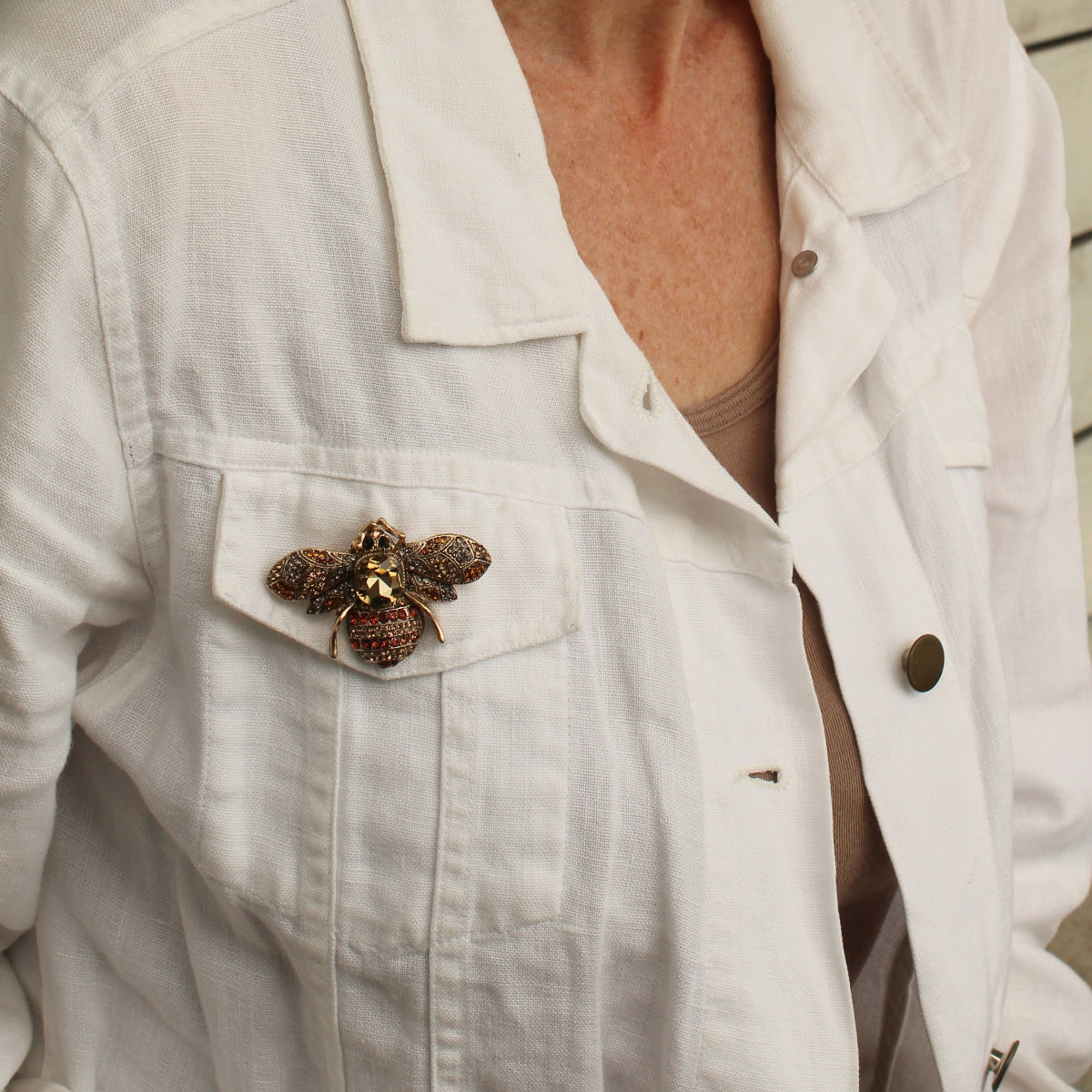 a close up of a woman wearing a white jacket and a bee broch in brown tones and sparkly crystals