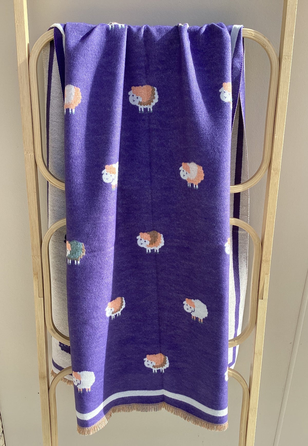 A purple winter scarf with a sheep pattern draped over a light wood frame. frame.
