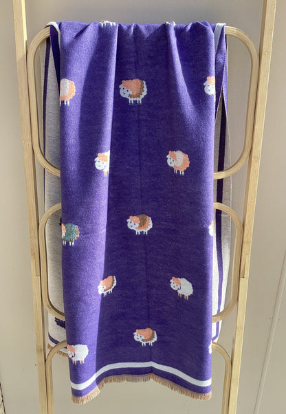 A purple winter scarf with a sheep pattern draped over a light wood frame. frame.