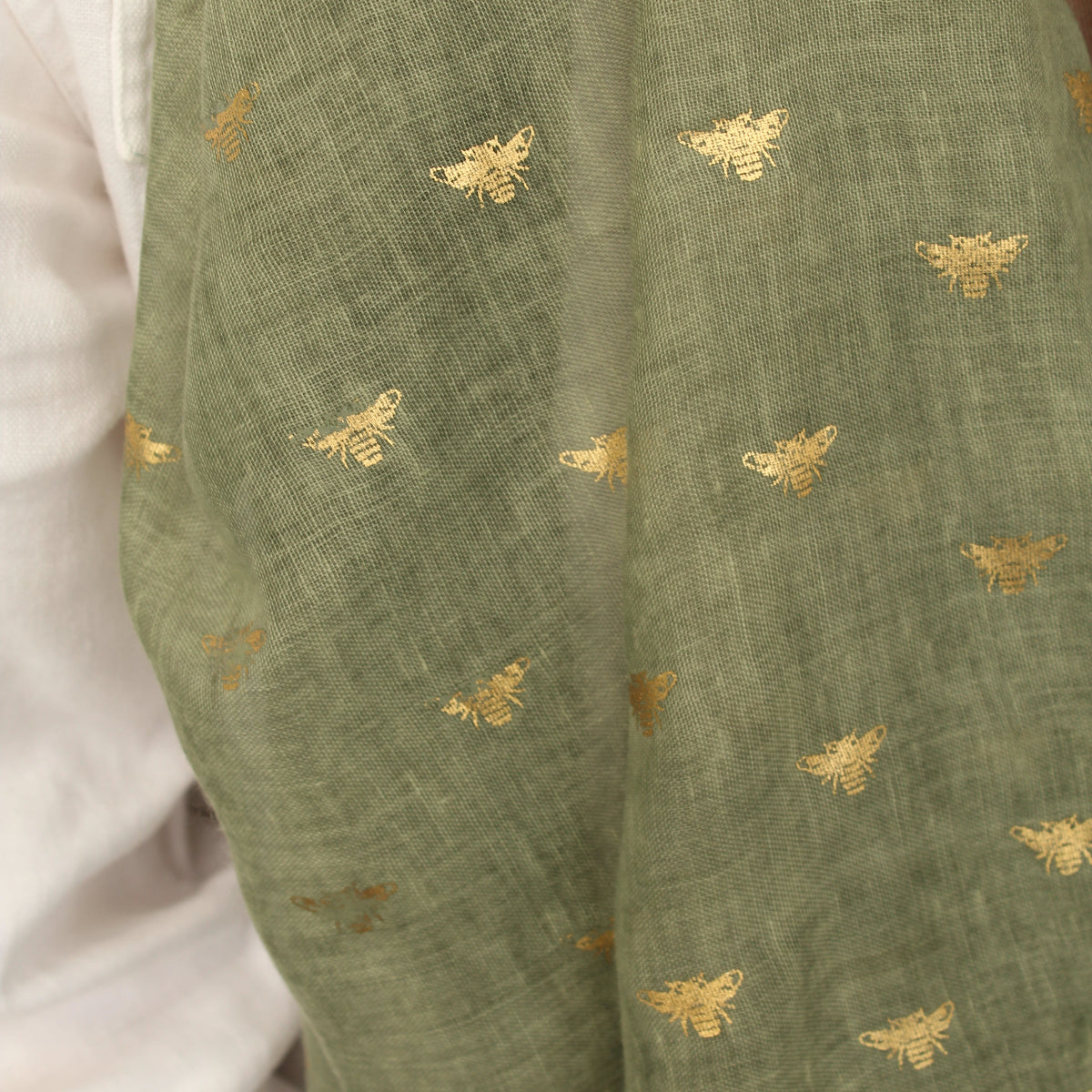 Olive green fabric with a delicate gold embroidered pattern of small bees, draped over a white garment.