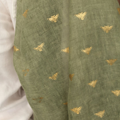 Olive green fabric with a delicate gold embroidered pattern of small bees, draped over a white garment.
