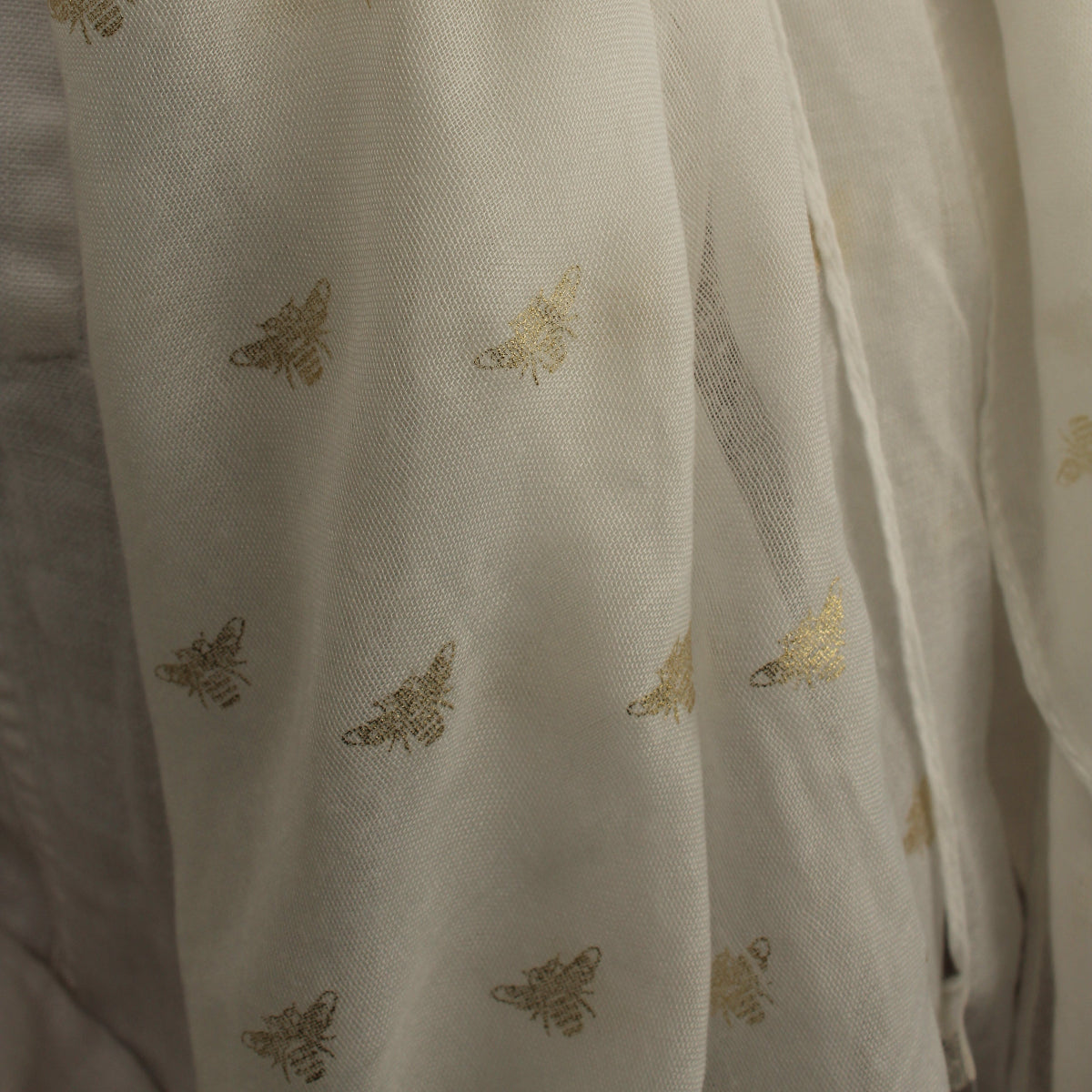 A close-up of a semi-sheer off-white  scarf, decorated with a repeating pattern of metallic gold butterflies.