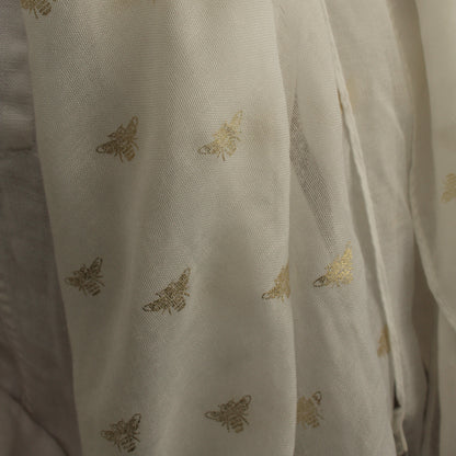 A close-up of a semi-sheer off-white  scarf, decorated with a repeating pattern of metallic gold butterflies.