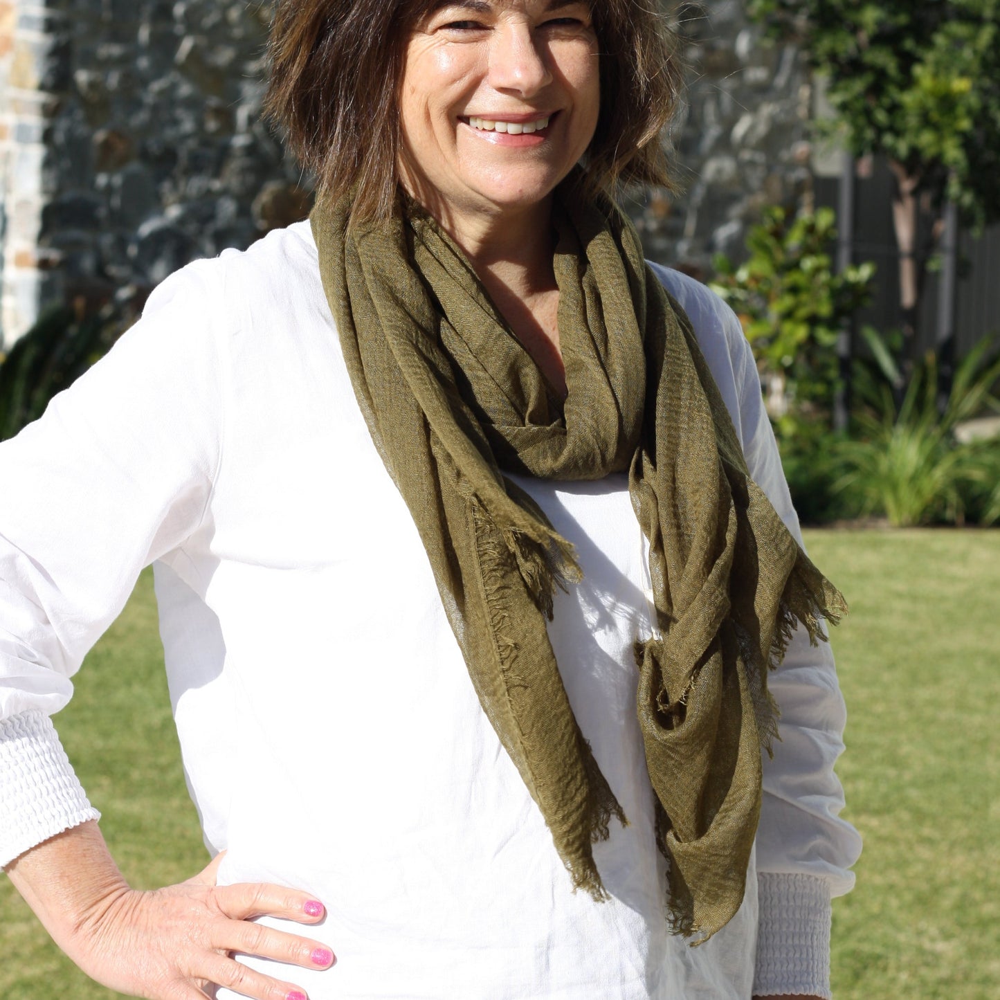 a lady wearing a plain dark olive green scarf that has a textured weave and a frayed edge on all sides.