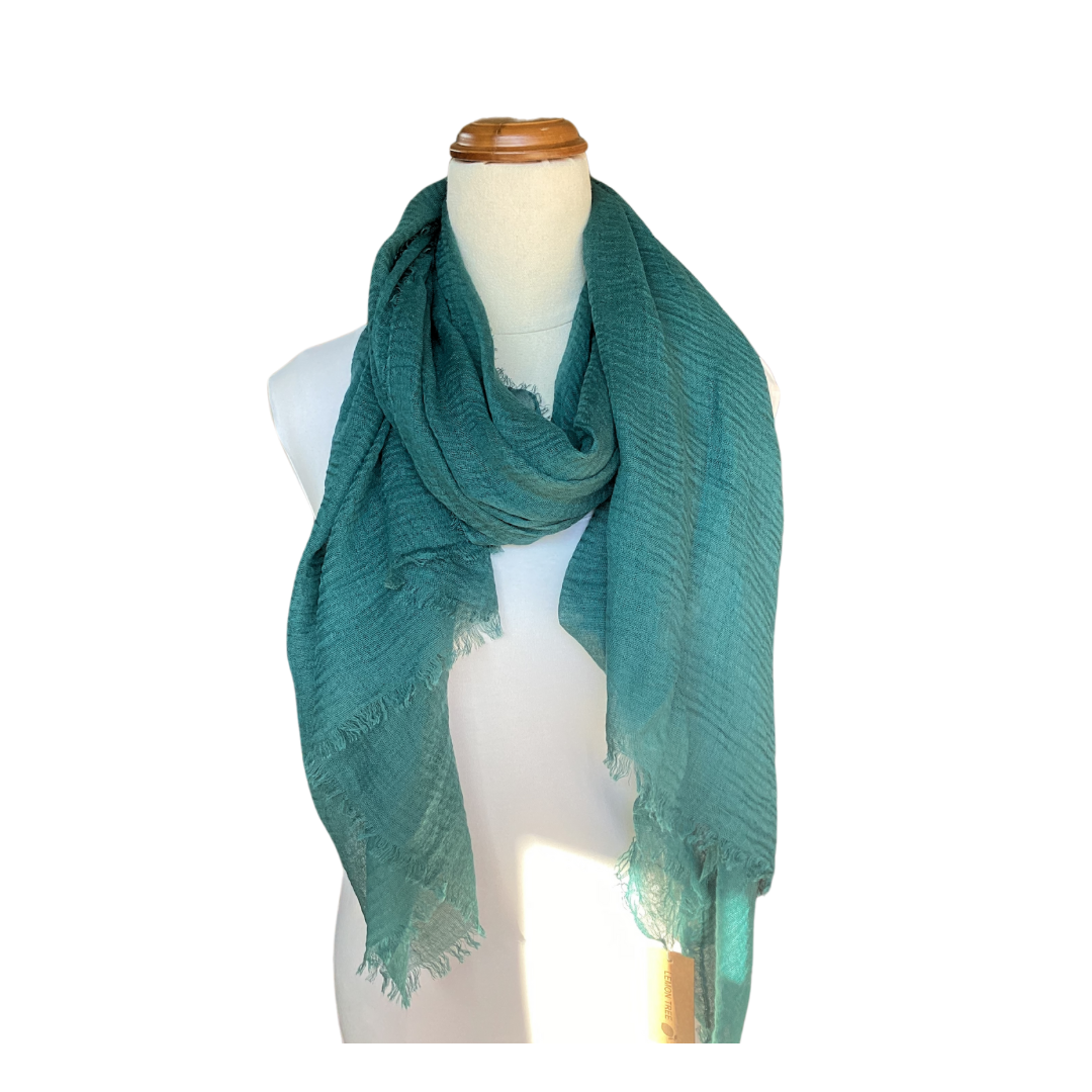 A mannequin wearing a dark green teal scarf. The scarf is plain but it has a textured weave and a frayed edge on all sides.