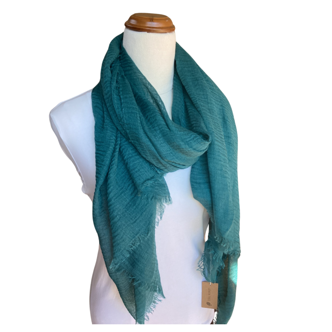 A mannequin wearing a dark green teal scarf. The scarf is plain but it has a textured weave and a frayed edge on all sides.