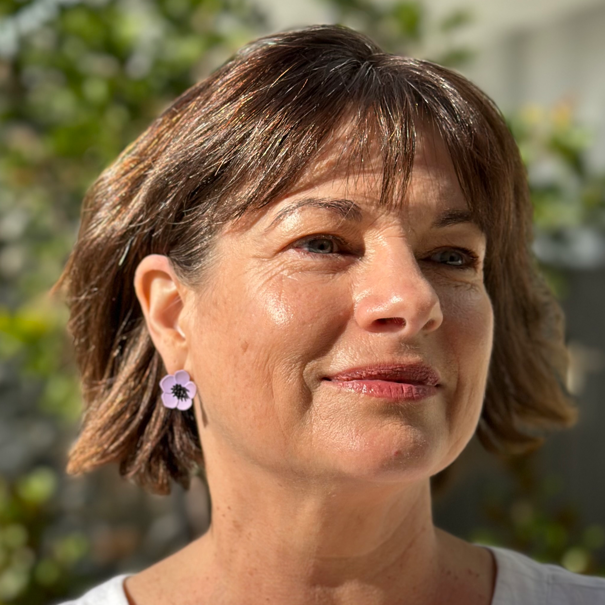 Lady wearing purple flower earrings  made from polymer clay with a black centre