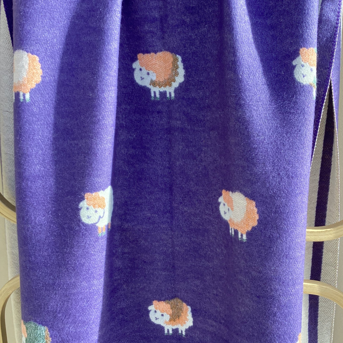 Purple scarf with a repeating pattern of sheep in orange, white, and purple draped over a wooden rack.