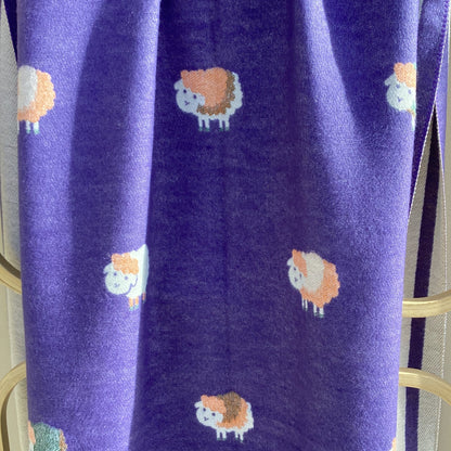 Purple scarf with a repeating pattern of sheep in orange, white, and purple draped over a wooden rack.