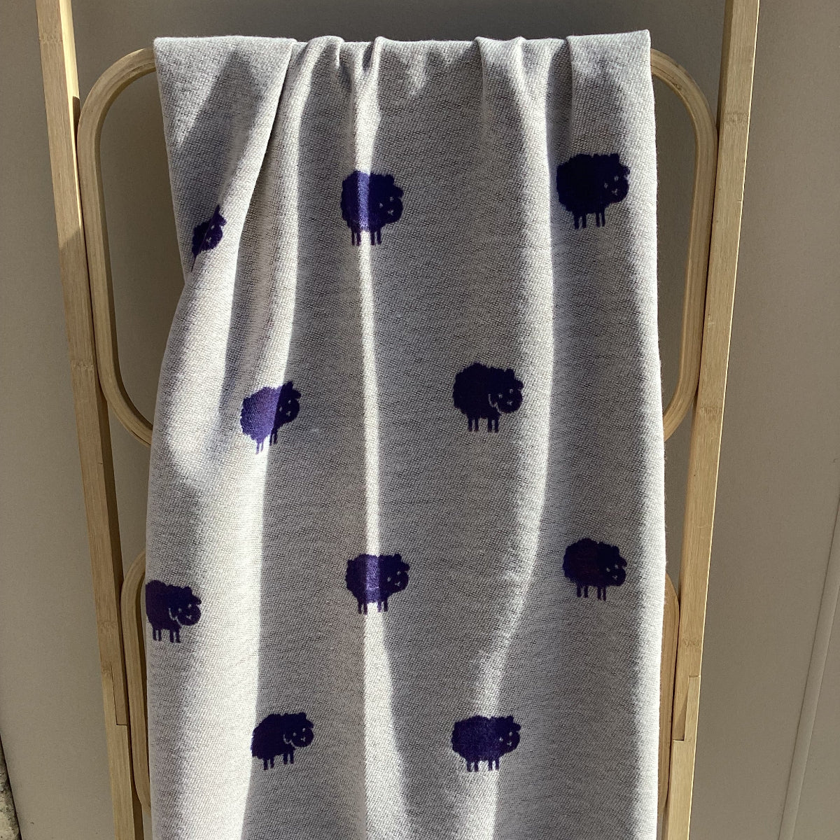 a beige winter scarf with purple sheep pattern draped over a wooden rack