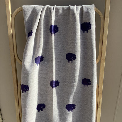 a beige winter scarf with purple sheep pattern draped over a wooden rack