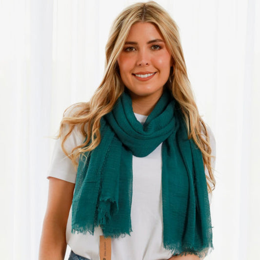 a lady wearing a dark green teal scarf. The scarf is plain but it has a textured weave and a frayed edge on all sides.