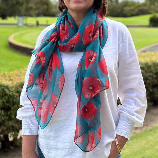 a lady wearing a teal coloured scarf that has bright red poppy flowers