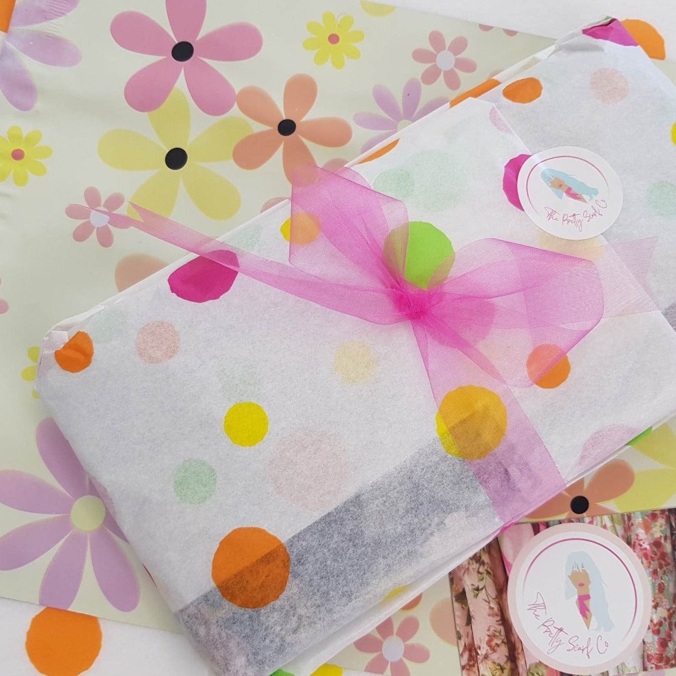 a ladies scarf gift wrapped in white tissue paper with pastel coloured spots and tied with a bright pink ribbon