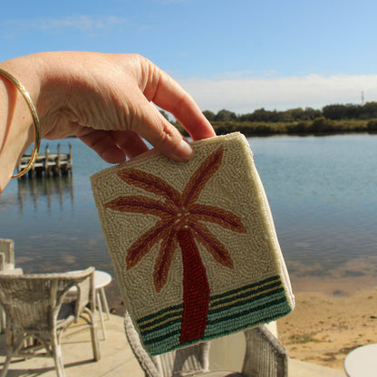 a hand holding a beaded zip purse with a white packground and a tropical palm tree