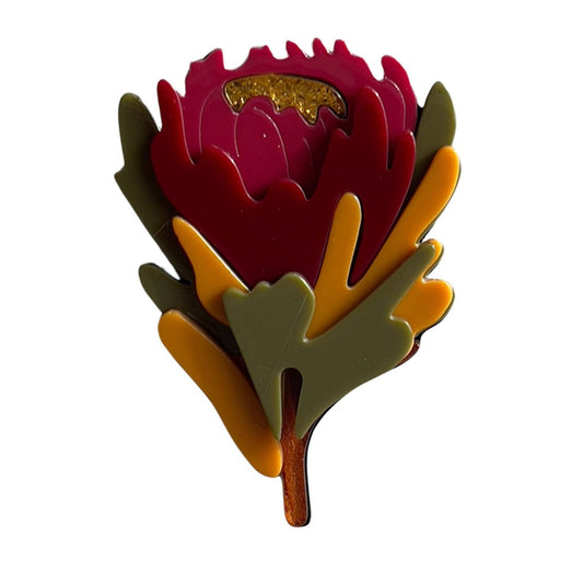 a brooch that has layers of leaves and a sparkly gold centre in the shape of a Waratah Flower