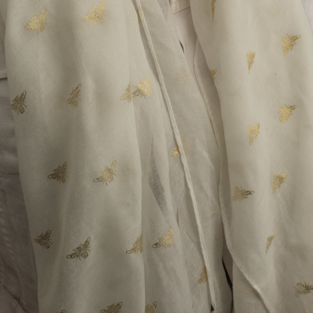 A close-up of a white scarf draped over a person's shoulders, featuring small scattered metallic gold butterfly motifs.