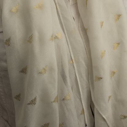 A close-up of a white scarf draped over a person's shoulders, featuring small scattered metallic gold butterfly motifs.